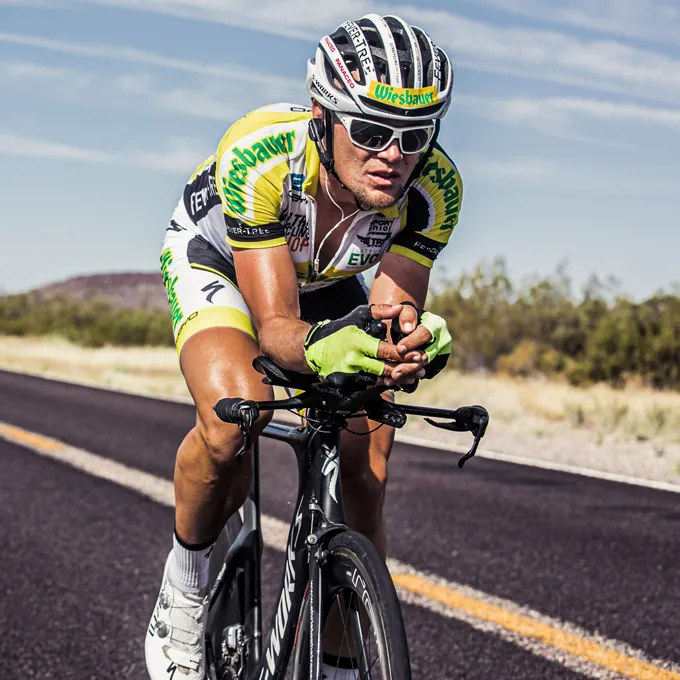 Un cycliste en maillot jaune et noir et des gants roule sur une route, portant un casque de cyclisme et des lunettes de soleil.