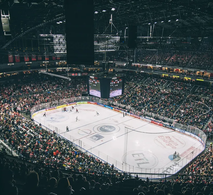 Une vue large d'une patinoire de hockey sur glace pleine, avec des joueurs sur la glace et un grand tableau d'affichage.
