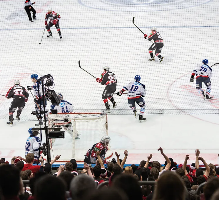 Une scène dynamique de hockey sur glace avec des joueurs en action sur la glace et une foule en arrière-plan qui acclame.