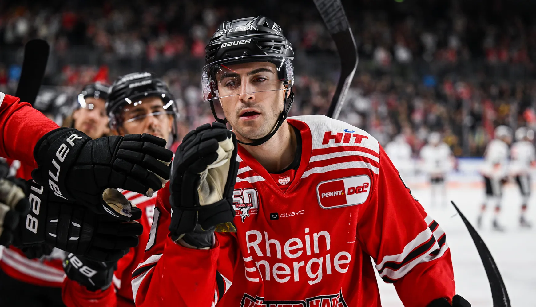 Un joueur de hockey en maillot rouge avec des rayures blanches et des gants, réagissant pendant le match.