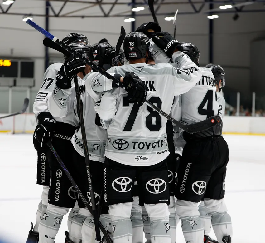 Joueurs de hockey sur glace en maillots blancs avec des numéros noirs et le logo Toyota célébrant sur la glace.