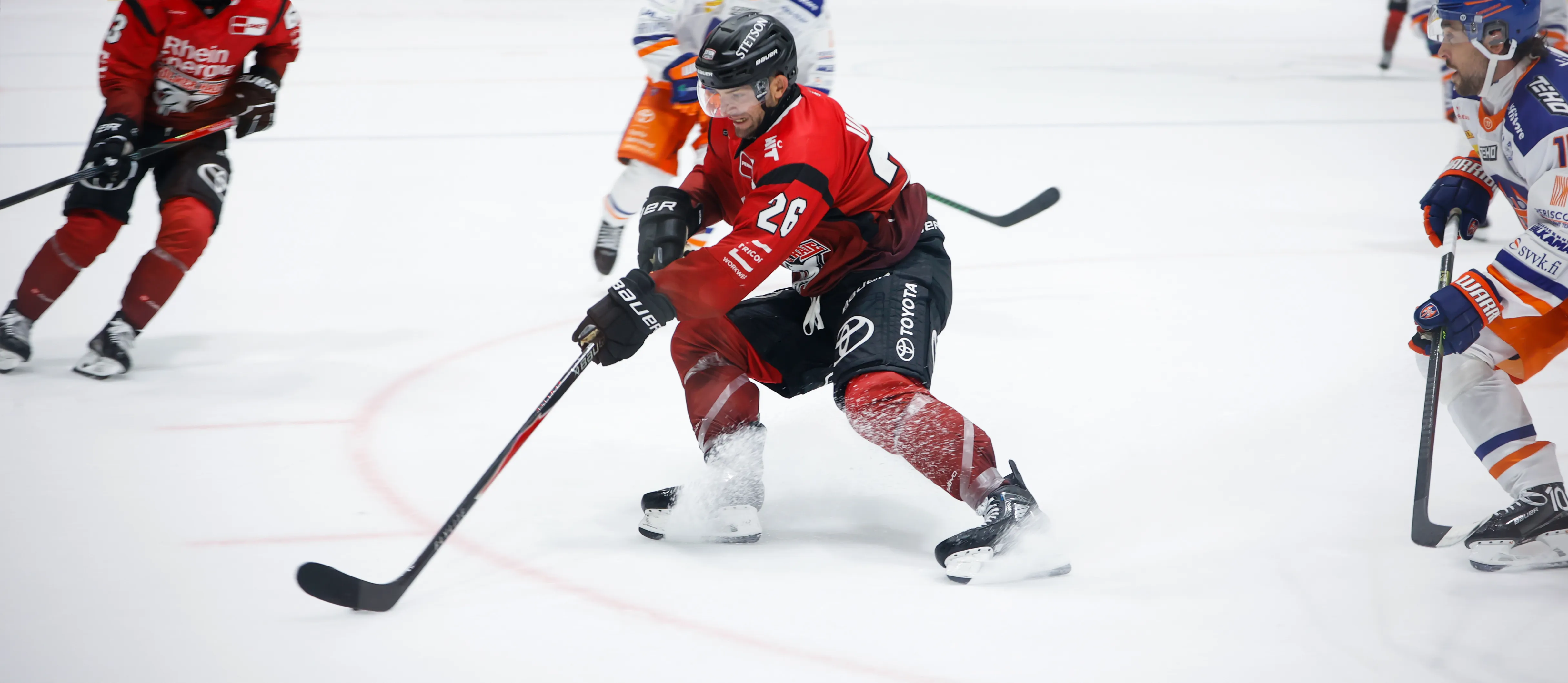 Un joueur de hockey sur glace en tenue de sport rouge dribble le palet sur la glace.