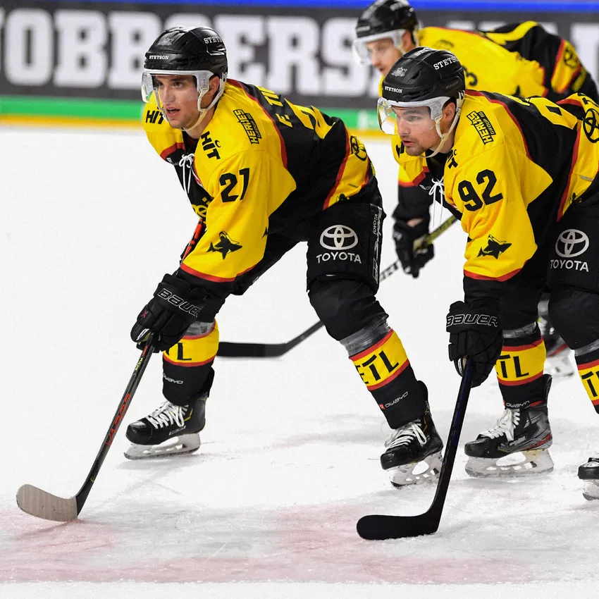 Deux joueurs de hockey sur glace en maillots jaune et noir sont sur la glace.