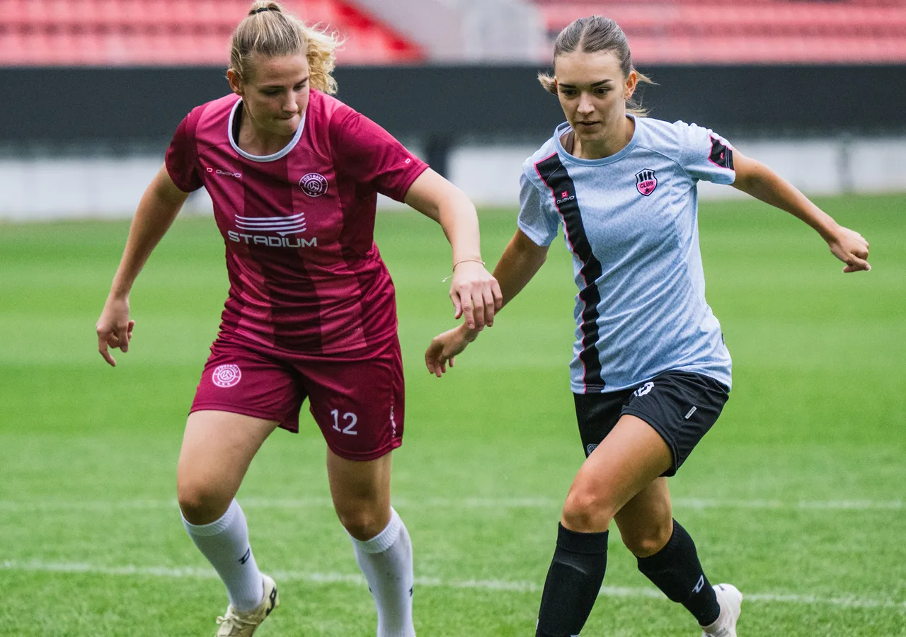 Deux femmes en tenue de sport jouent au football sur un terrain en herbe.