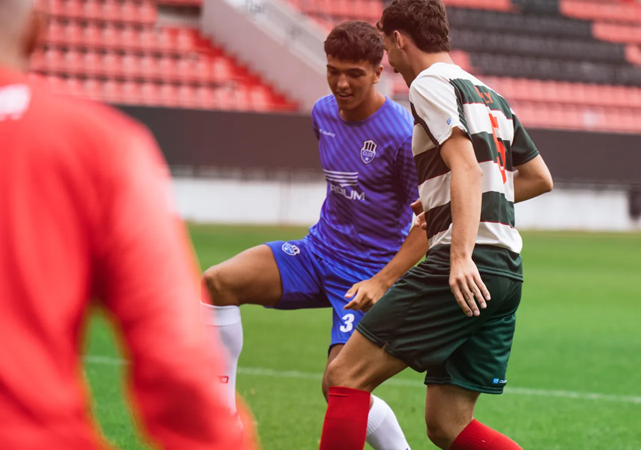 Deux footballeurs en action sur le terrain, l'un portant un maillot bleu et l'autre un maillot rayé.