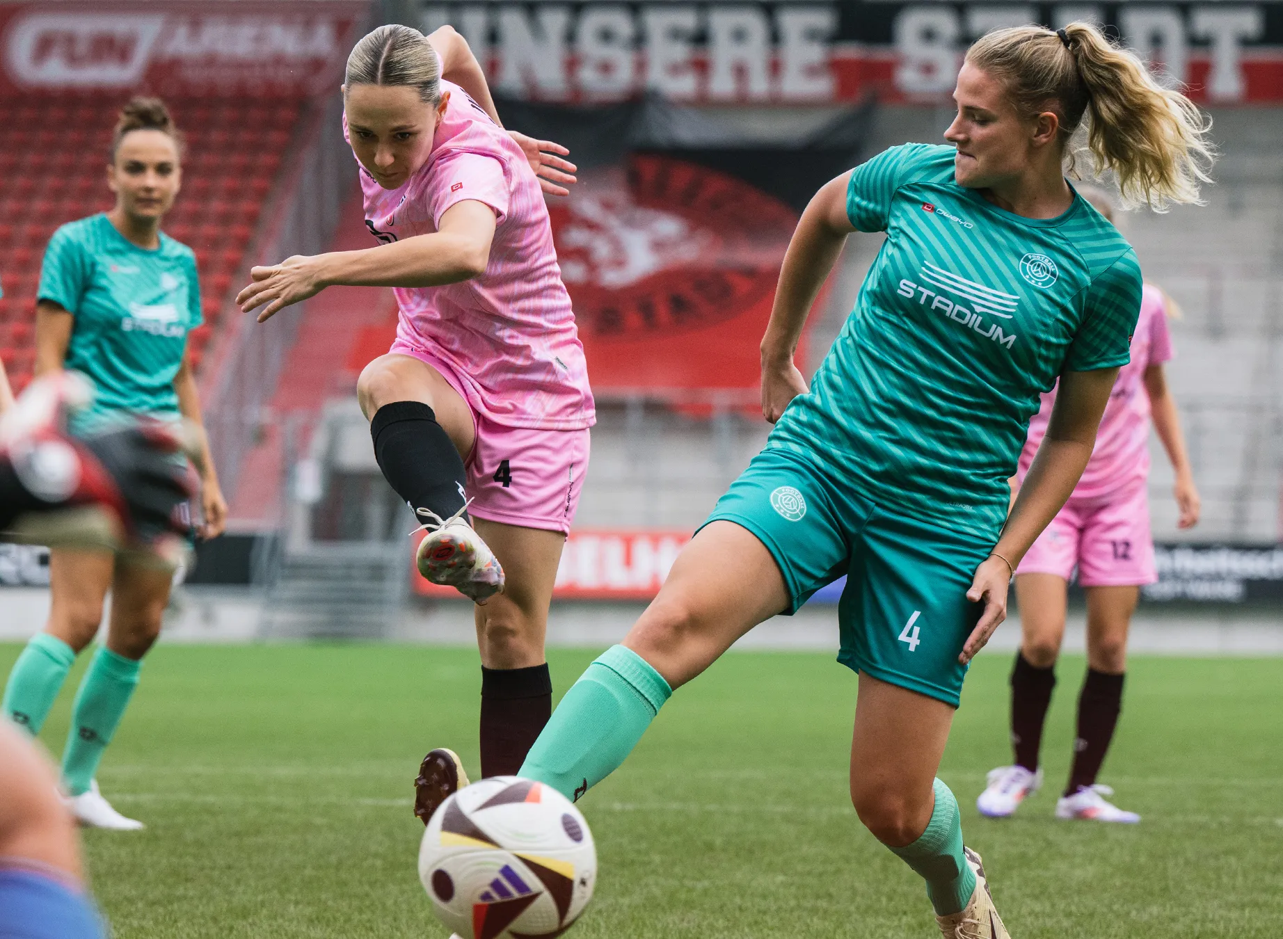 Deux femmes en maillots de sport colorés jouent au football sur un terrain en herbe.