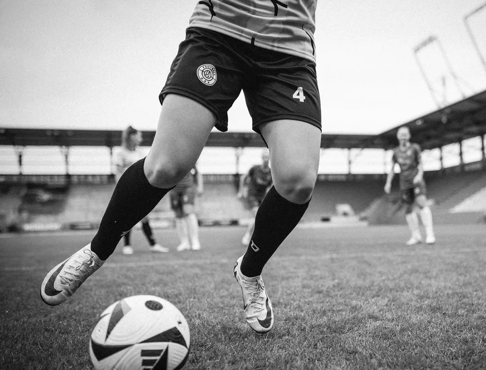 Une footballeuse en short et en chaussettes longues jouant avec un ballon sur le terrain.