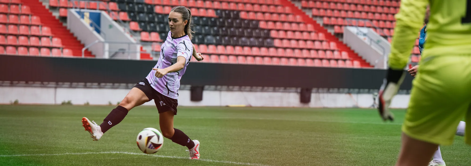 Une joueuse en maillot de football violet frappe le ballon sur un terrain en gazon.