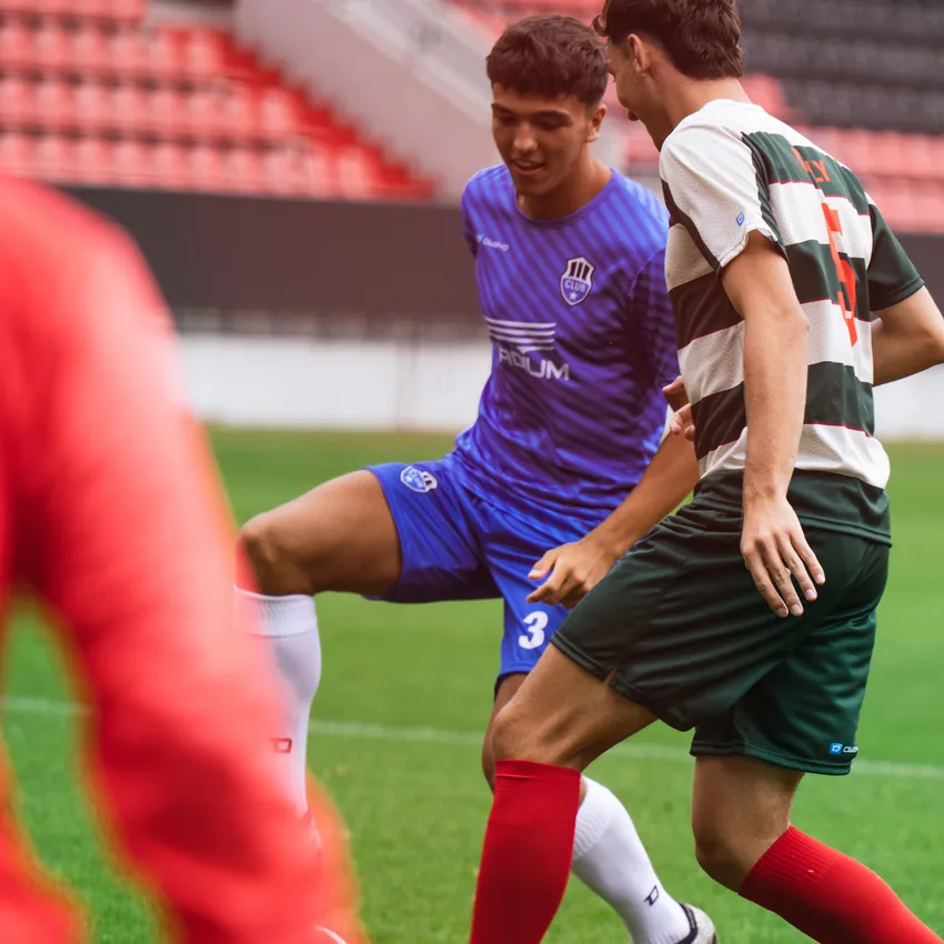 Deux joueurs de football en action, l'un portant un maillot bleu et l'autre un maillot rayé vert et blanc, se tenant sur un terrain de football.