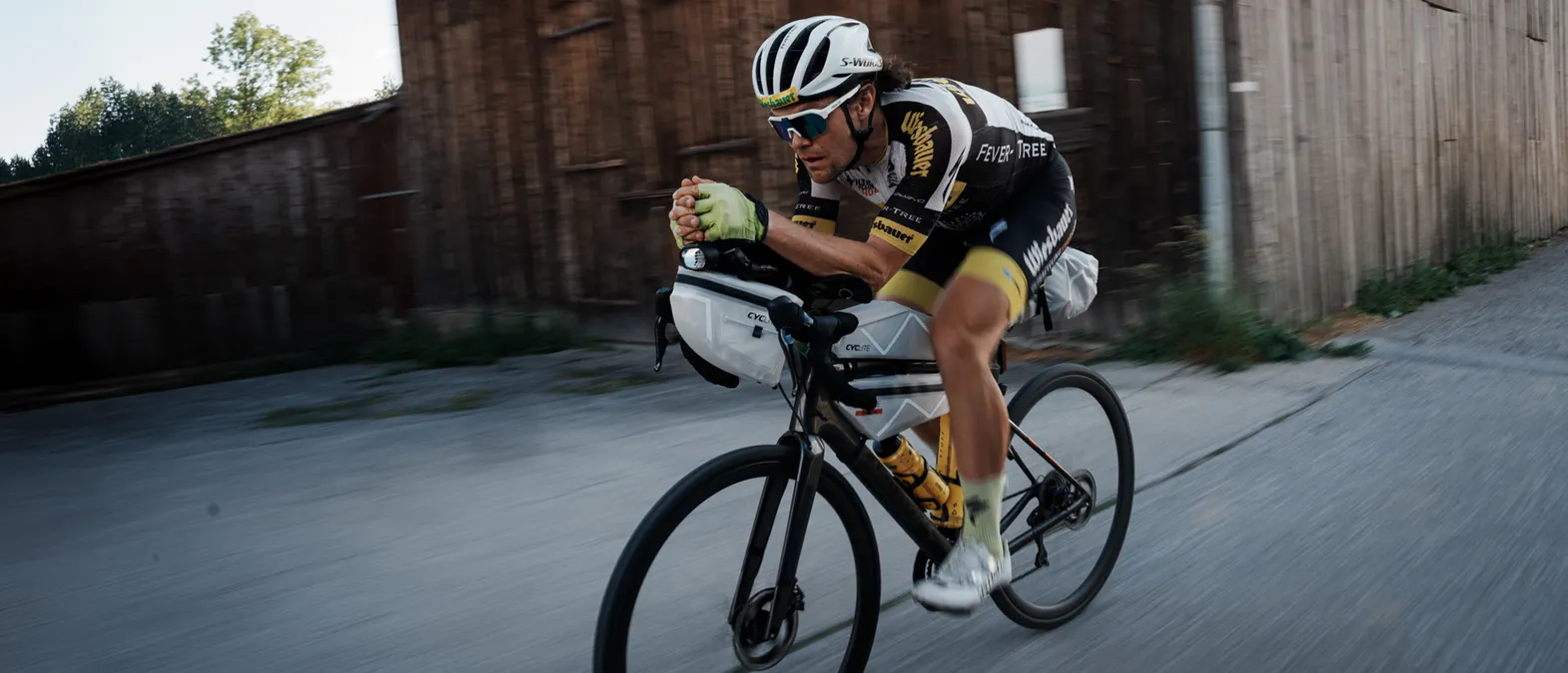 Un cycliste en position aérodynamique sur un vélo de route, portant une tenue de sport personnalisée d'owayo, en train de rouler sur une rue.