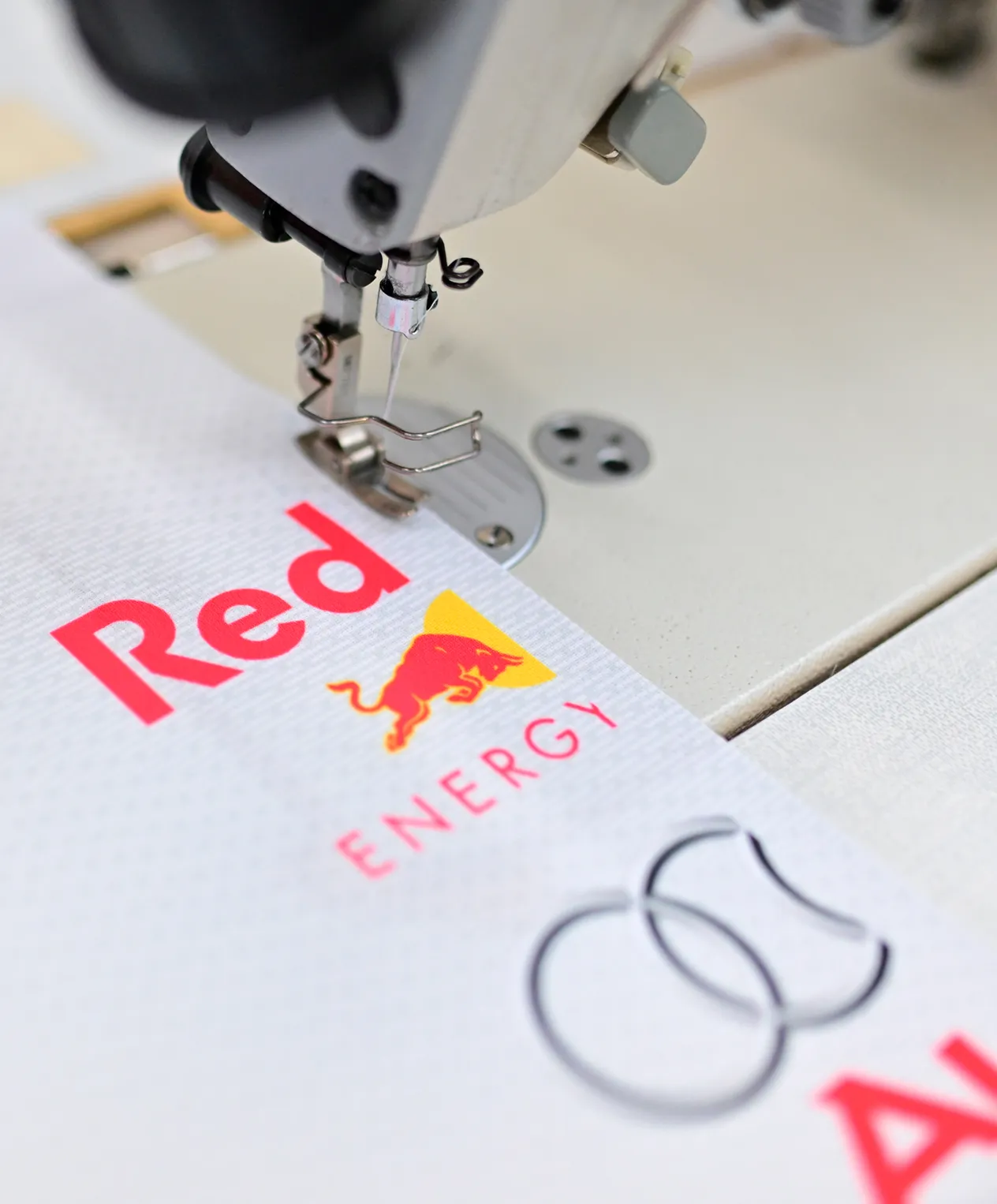 Une machine à coudre brode un vêtement de sport blanc avec le logo Red Bull Energy.