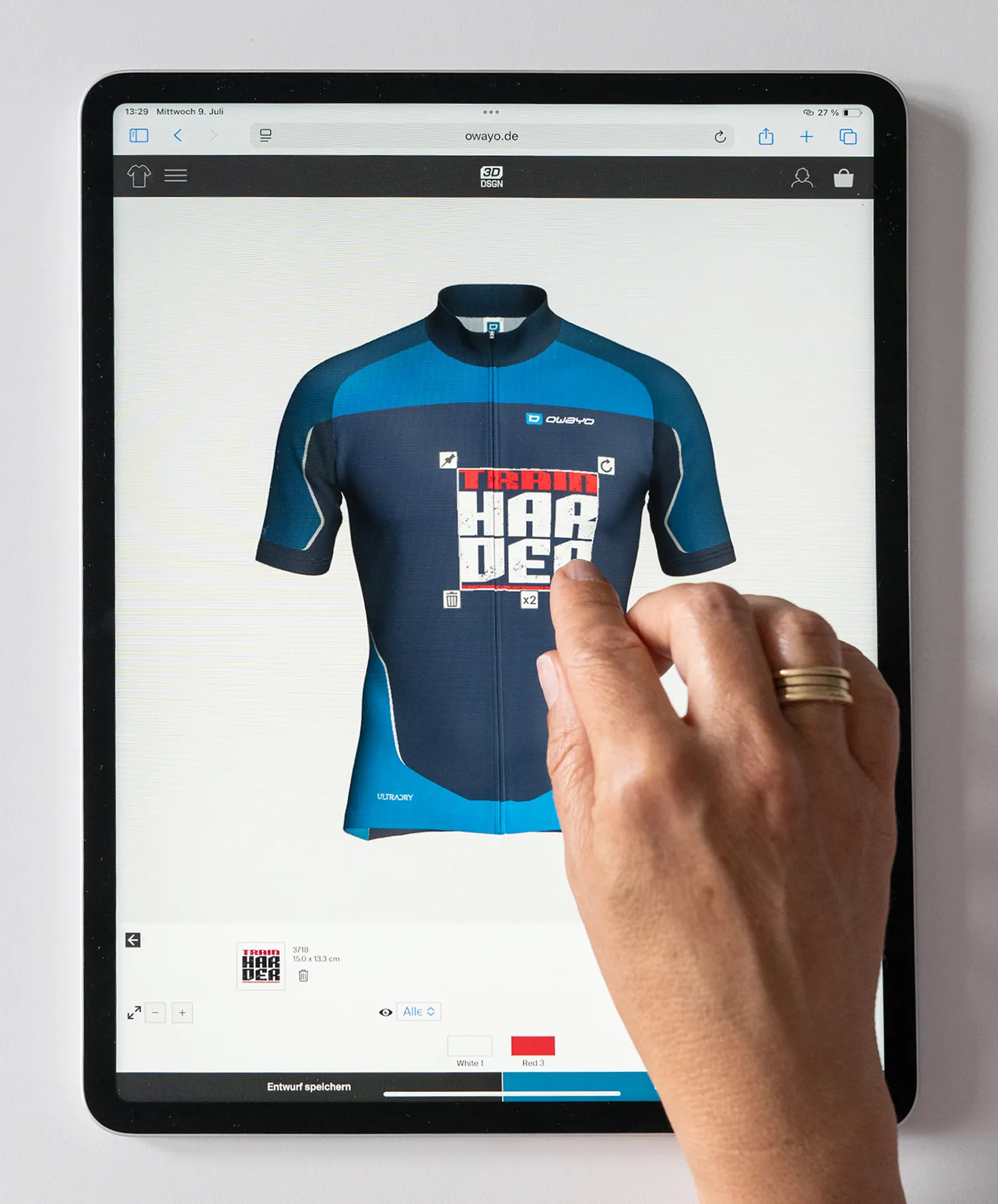 Une main interagit avec une tablette affichant le site web d'owayo, montrant un maillot de cyclisme personnalisé bleu et bleu foncé avec l'inscription 'TRAIN HARDER'.