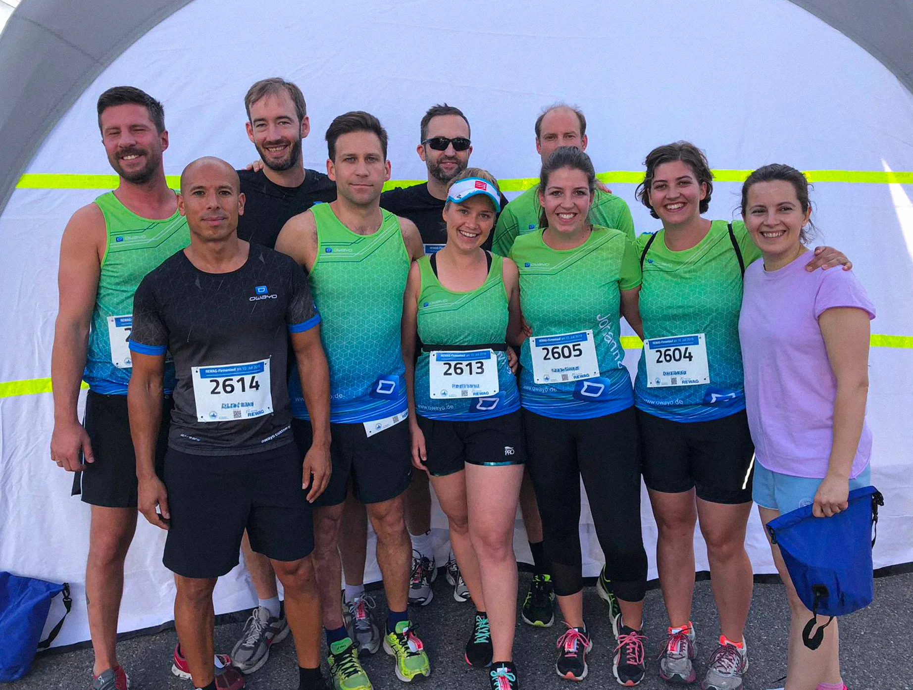 Un groupe de coureurs en vêtements de sport personnalisés d'owayo pose devant une tente, certains portant des dossards.