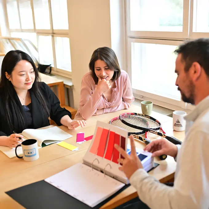 Trois personnes sont assises à une table en train de discuter des palettes de couleurs et des designs pour des vêtements de sport sur mesure.