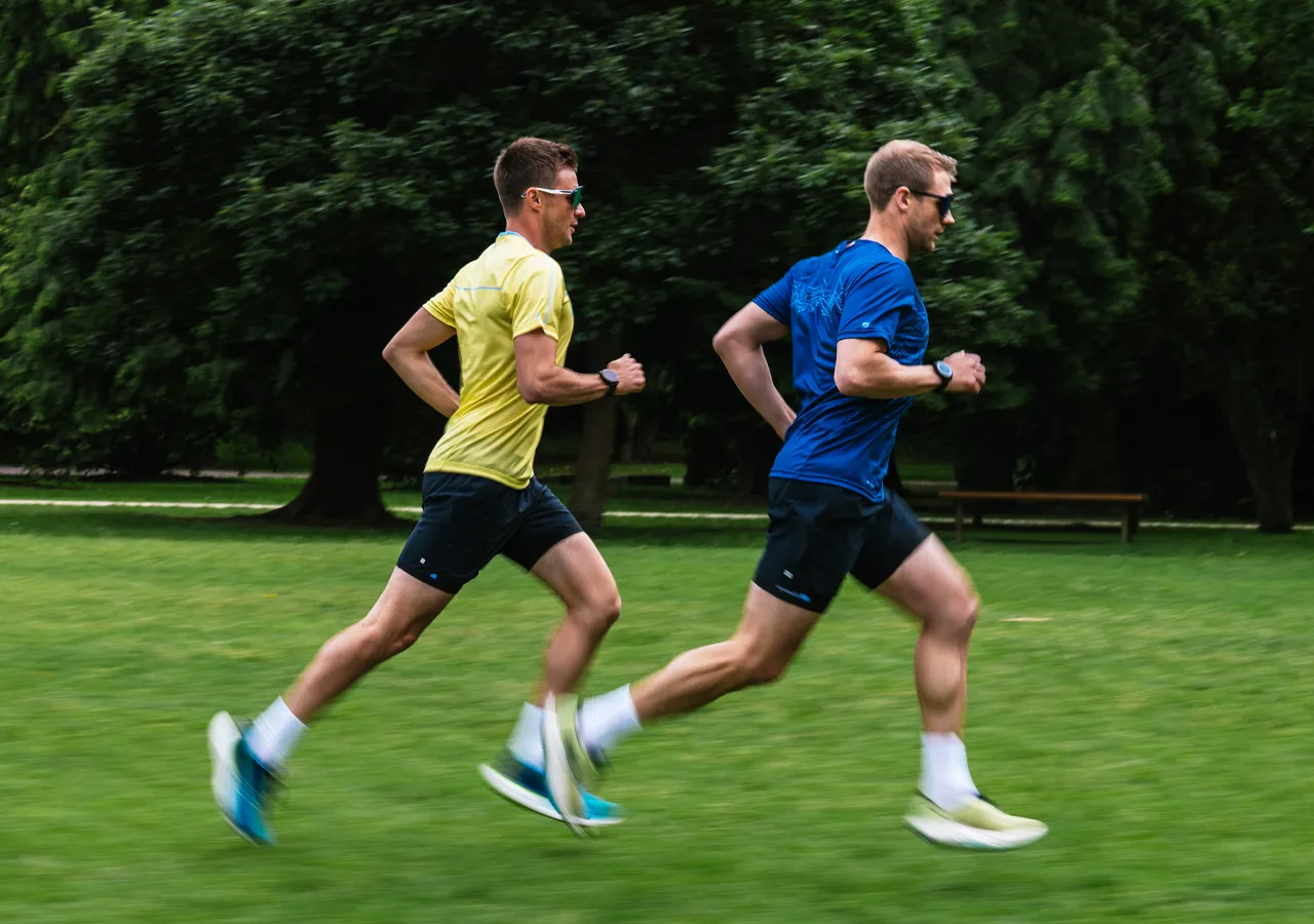 Deux coureurs en tenue de sport courent sur un champ vert.