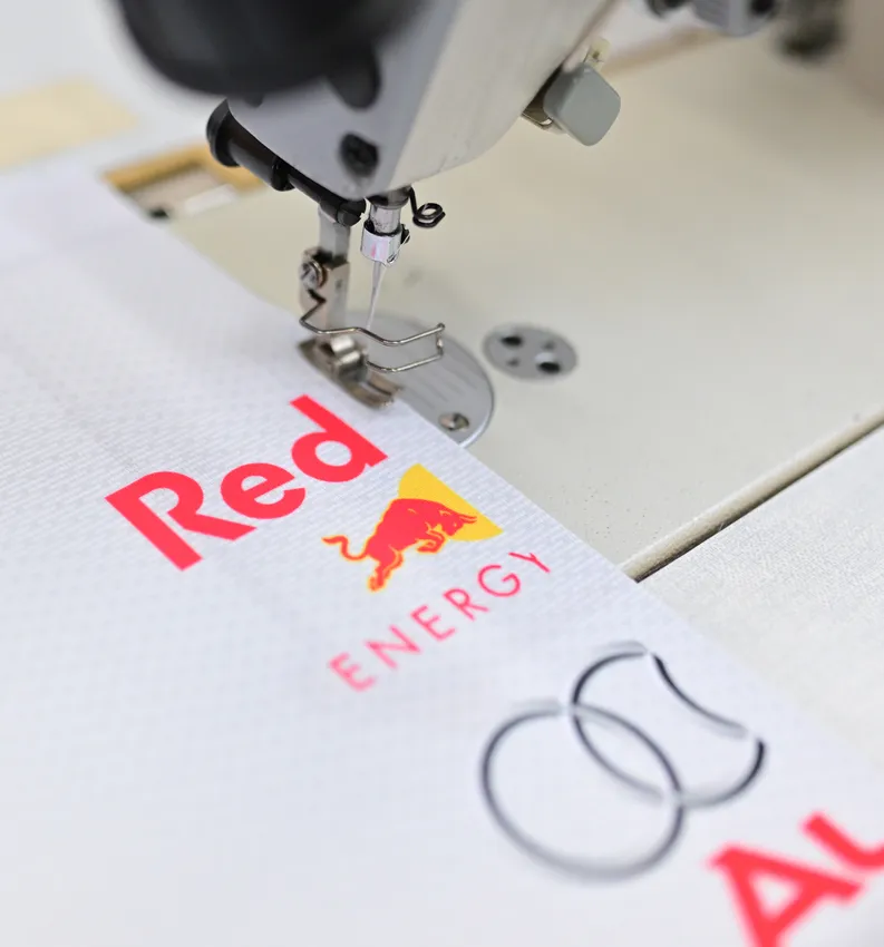 Une machine à coudre brode un vêtement sportif blanc avec le logo rouge Red Bull.