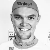 Un homme portant une tenue de cyclisme avec le logo 'Wiesbauer' sur la casquette et le maillot.