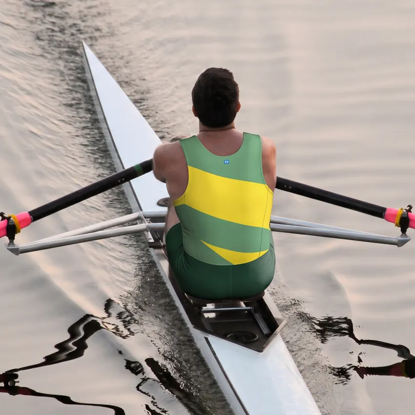 Un rameur portant une combinaison une pièce verte et jaune rame sur une eau calme.