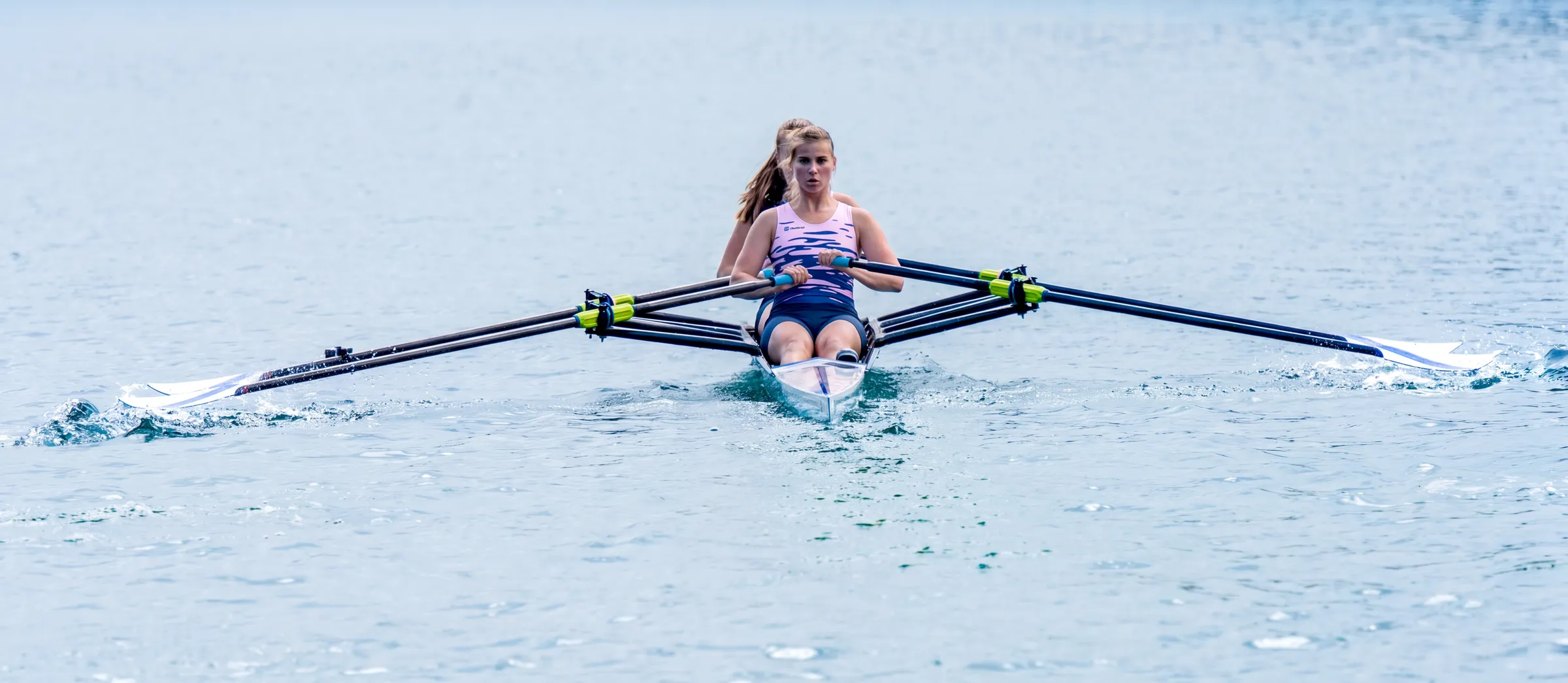 Une rameuse pagaye dans un skiff sur une eau calme.