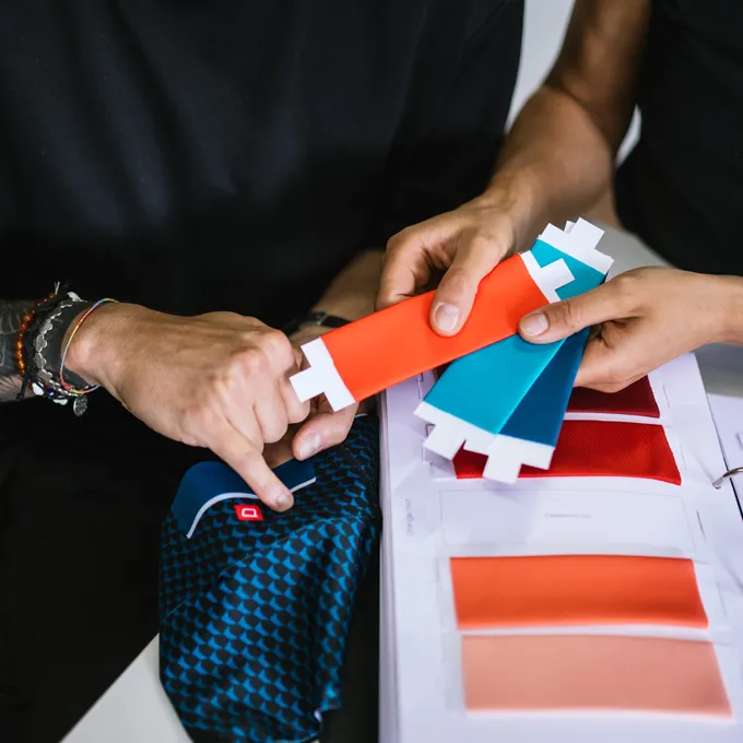 Deux personnes choisissent des échantillons de couleurs pour des vêtements de sport personnalisés, avec un tissu bleu à motif et plusieurs teintes visibles.